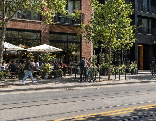People at outdoor cafe tables and walking past on a sunny street - illustrative context
