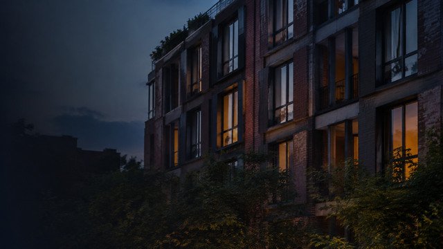 A dark apartment building at dusk, lit windows behind trees - illustrative context